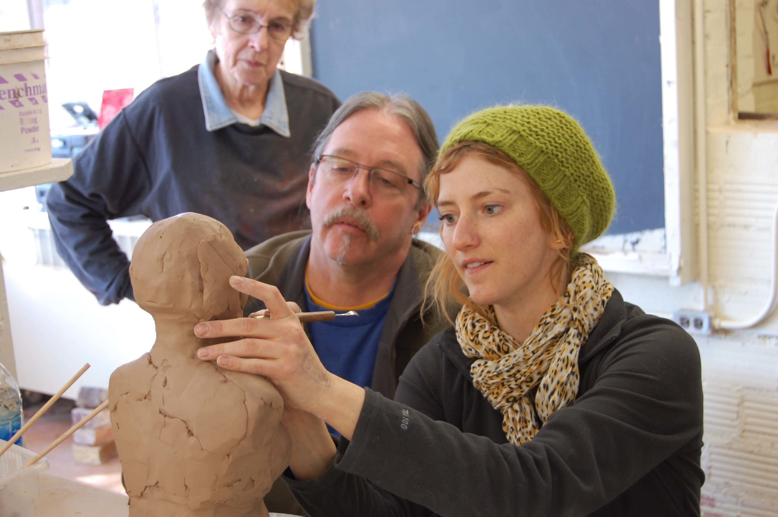 People look on as artist sculpts in clay