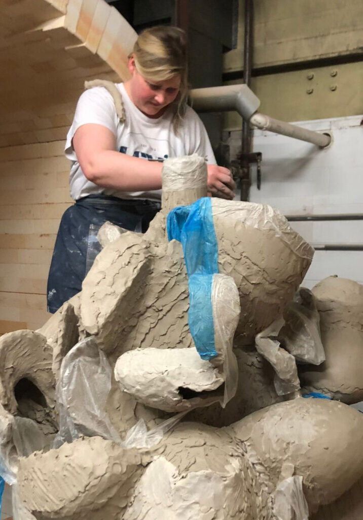 Laura Dirksen working on large sculpture while standing inside kiln door